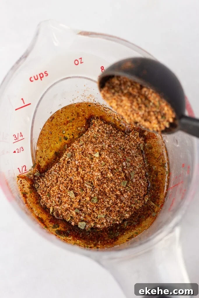 Close up of taco seasoning being dumped into a measuring cup that has oil and lime juice in it.