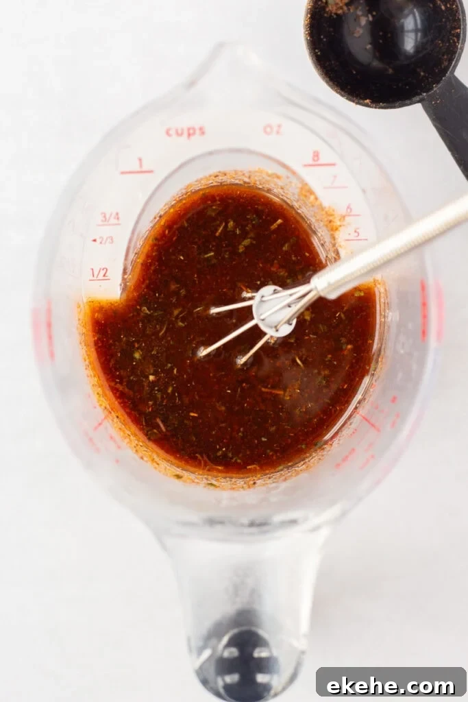 Top down close up of a measuring cup with a red taco marinade in it. A small whisk is in the cup as well, which rests on an off-white surface.