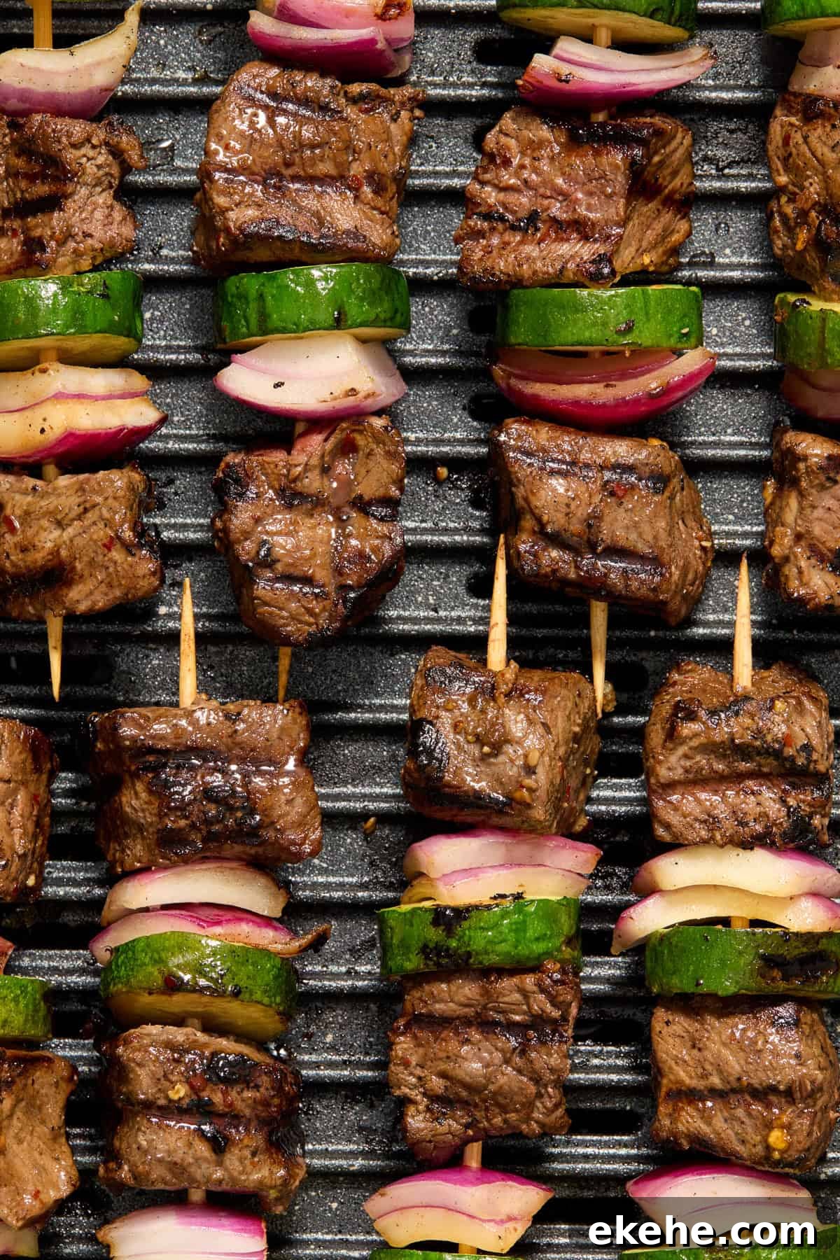 Grilled steak kabobs arranged in rows on grill.