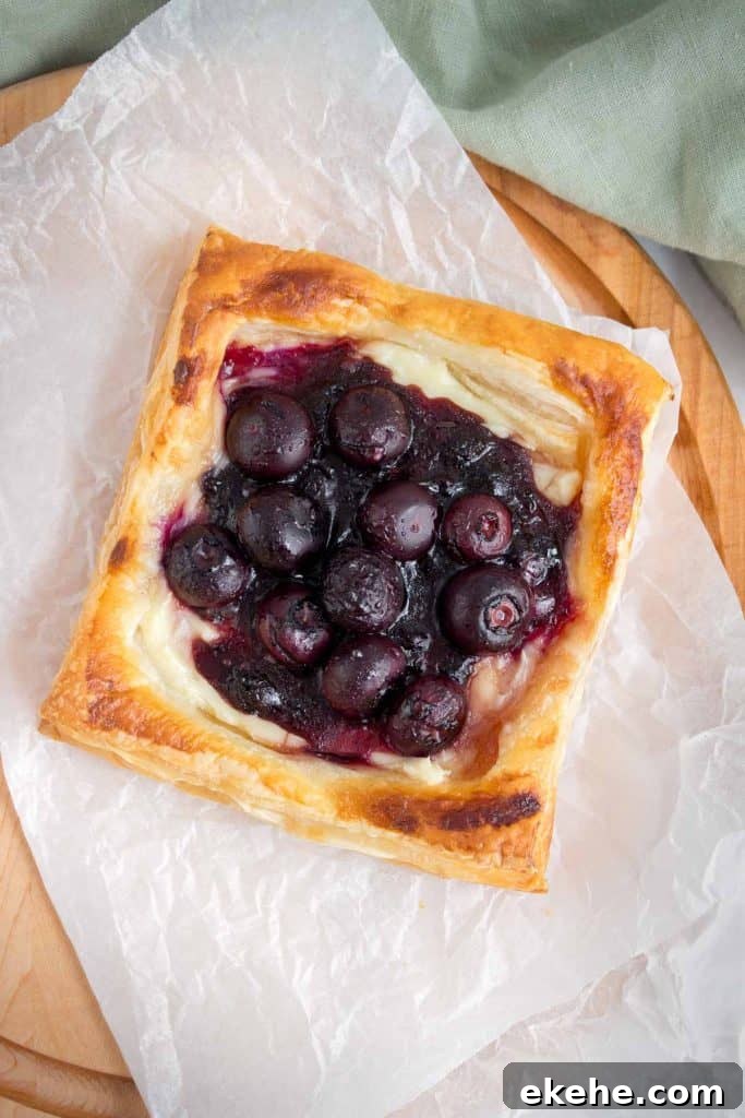 A blueberry danish on a parchment paper on a cutting board.
