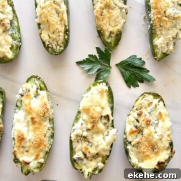 Baked stuffed jalapeños filled with feta, topped with breadcrumbs, arranged on a white surface, accompanied by a parsley leaf.