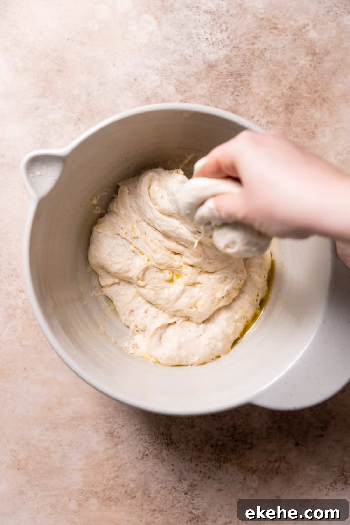a hand stretching and folding the focaccia dough in a bowl.