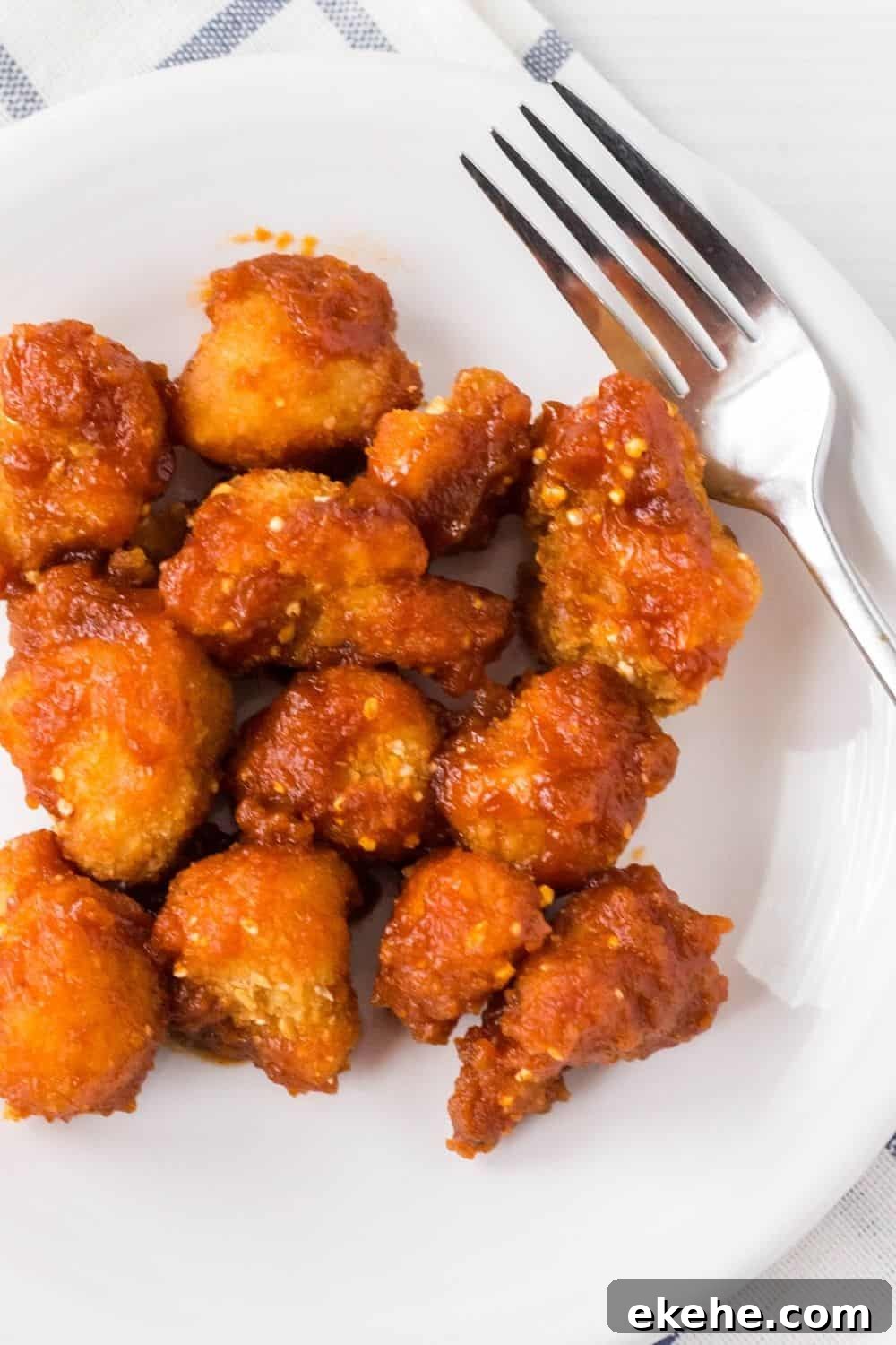air fryer frozen cauliflower wings tossed in sauce and served in a white plate with a fork next to them