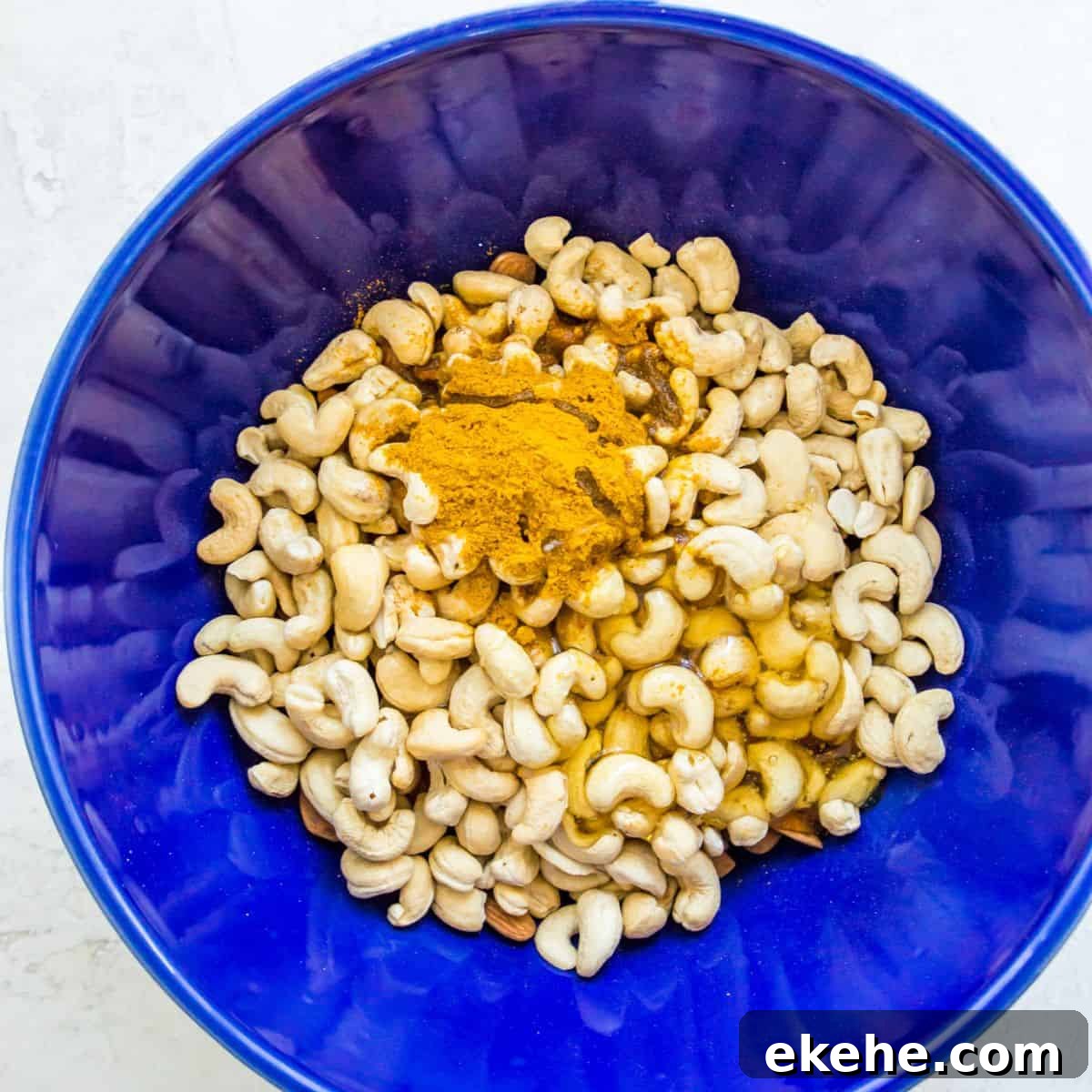 Sweet Curry-Glazed Cashews & Almonds: Spiced Snack Recipe 4 A blue bowl filled with cashews, almonds, curry spice and honey.