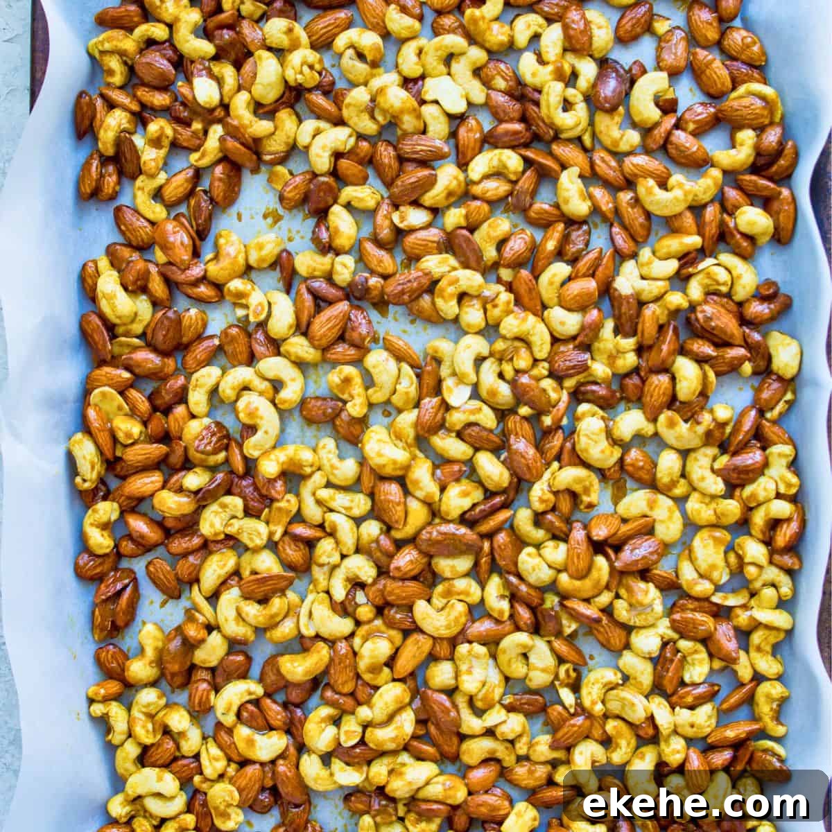 Sweet Curry-Glazed Cashews & Almonds: Spiced Snack Recipe 6 A baking sheet lined with parchment paper with cashews and almonds spread over it.