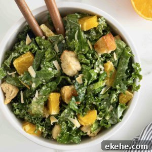 A white salad bowl of citrus caesar salad. Two wooden spoon handles are sticking out.