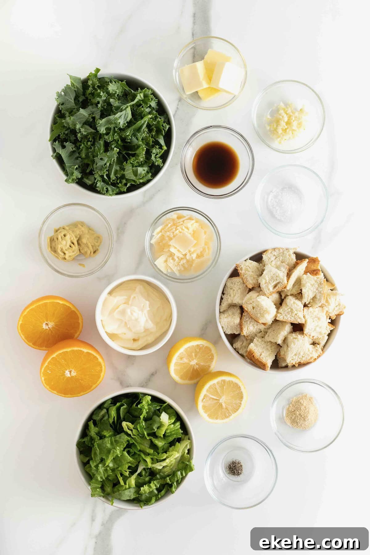 Ingredients to make citrus caesar salad in small glass dishes on a white marble counter.