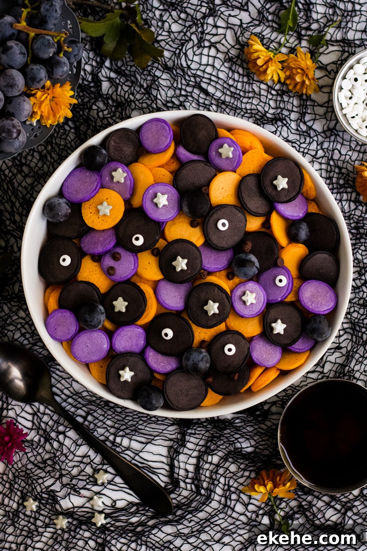 A bowl of purple, orange and black mini Halloween pancakes with candy eyes and stars.