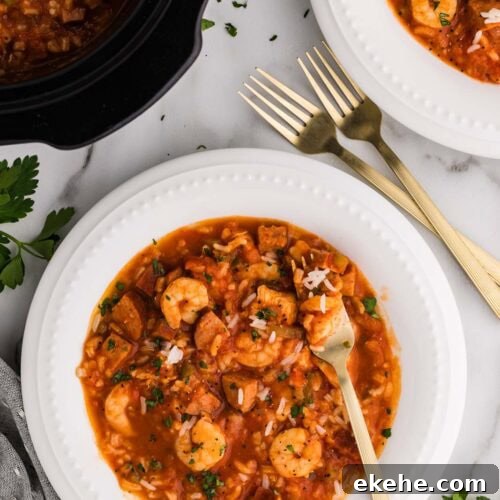 overhead view of 2 dinner bowls of jambalaya with forks with black slow cooker of jambalaya in background