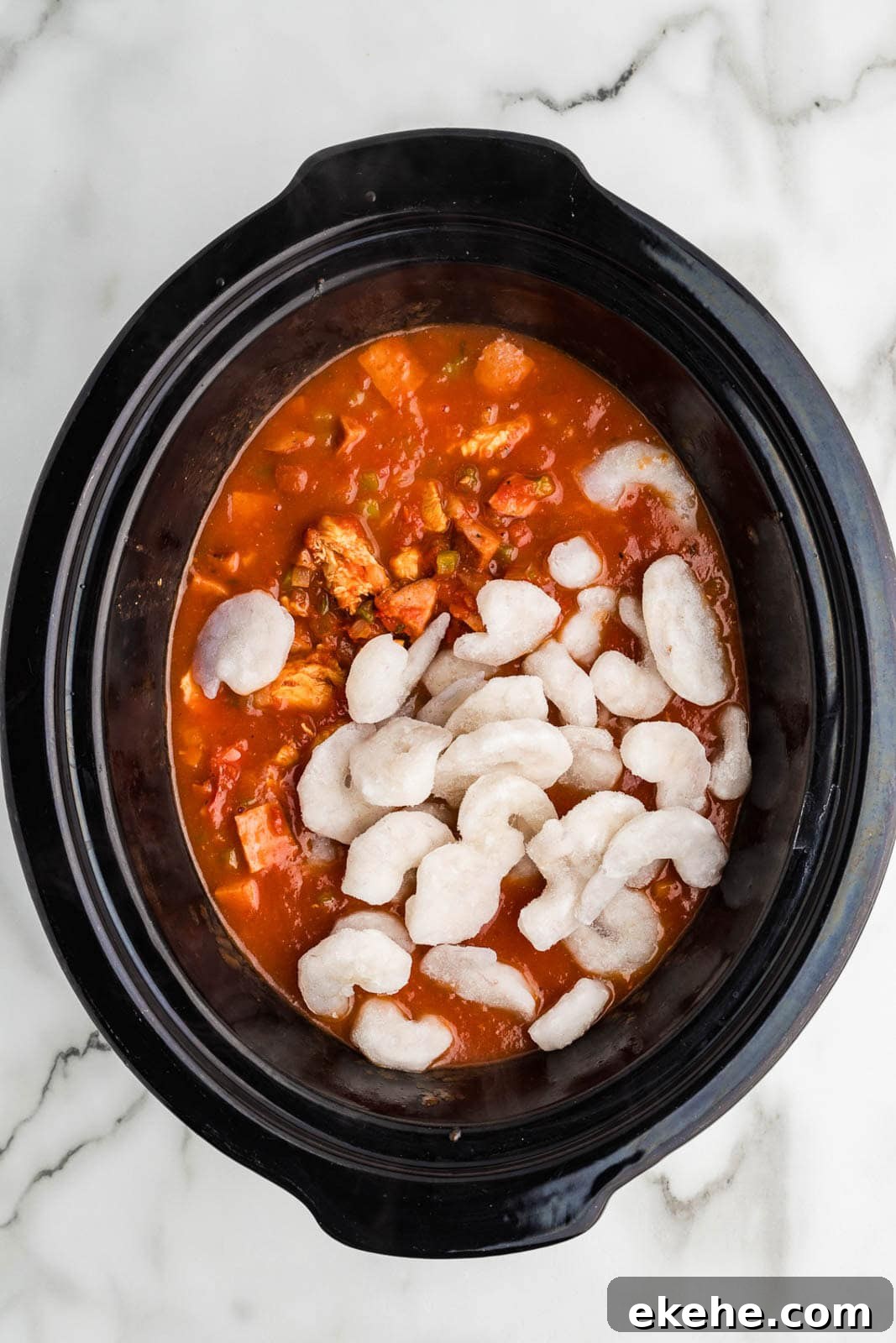 black slow cooker of cooked mixture with raw shrimp added on top