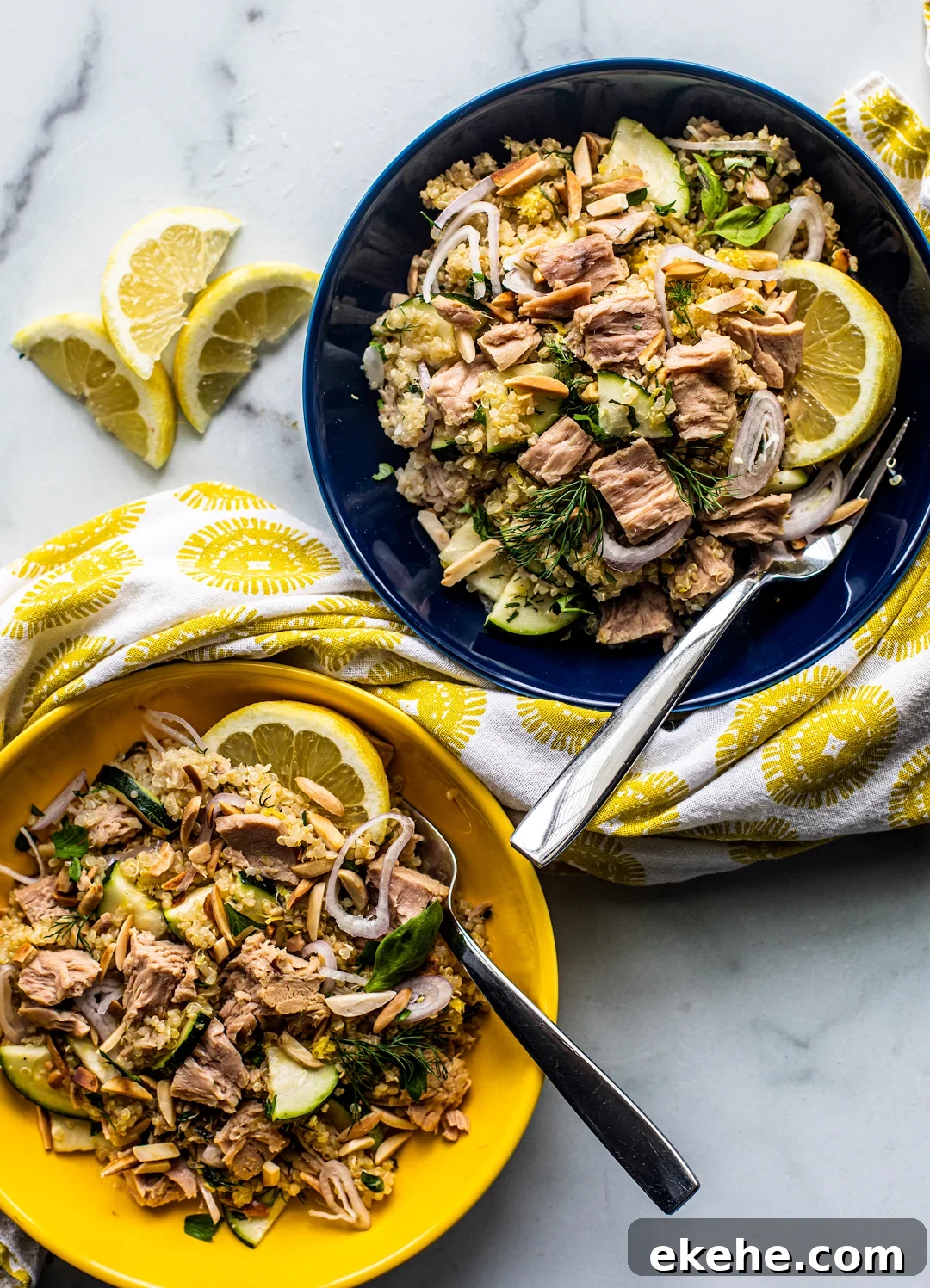 Two bowls of quinoa topped with large flakes of tuna and lemon wedges.