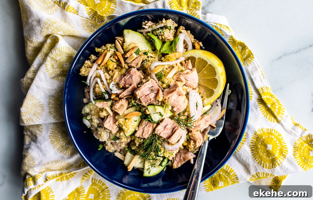 Bowl of quinoa salad topped with tuna and lemon wedges.
