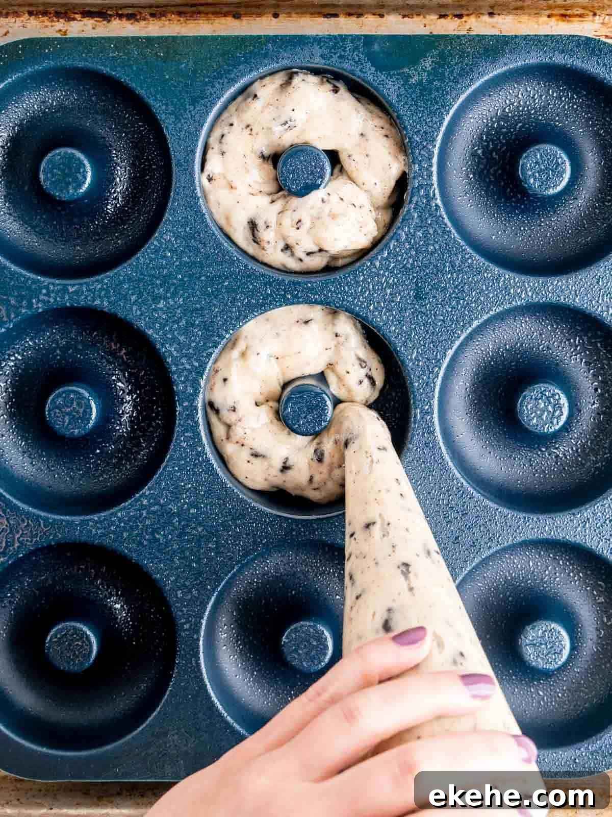 Piping cookies and cream donut batter into a donut pan.