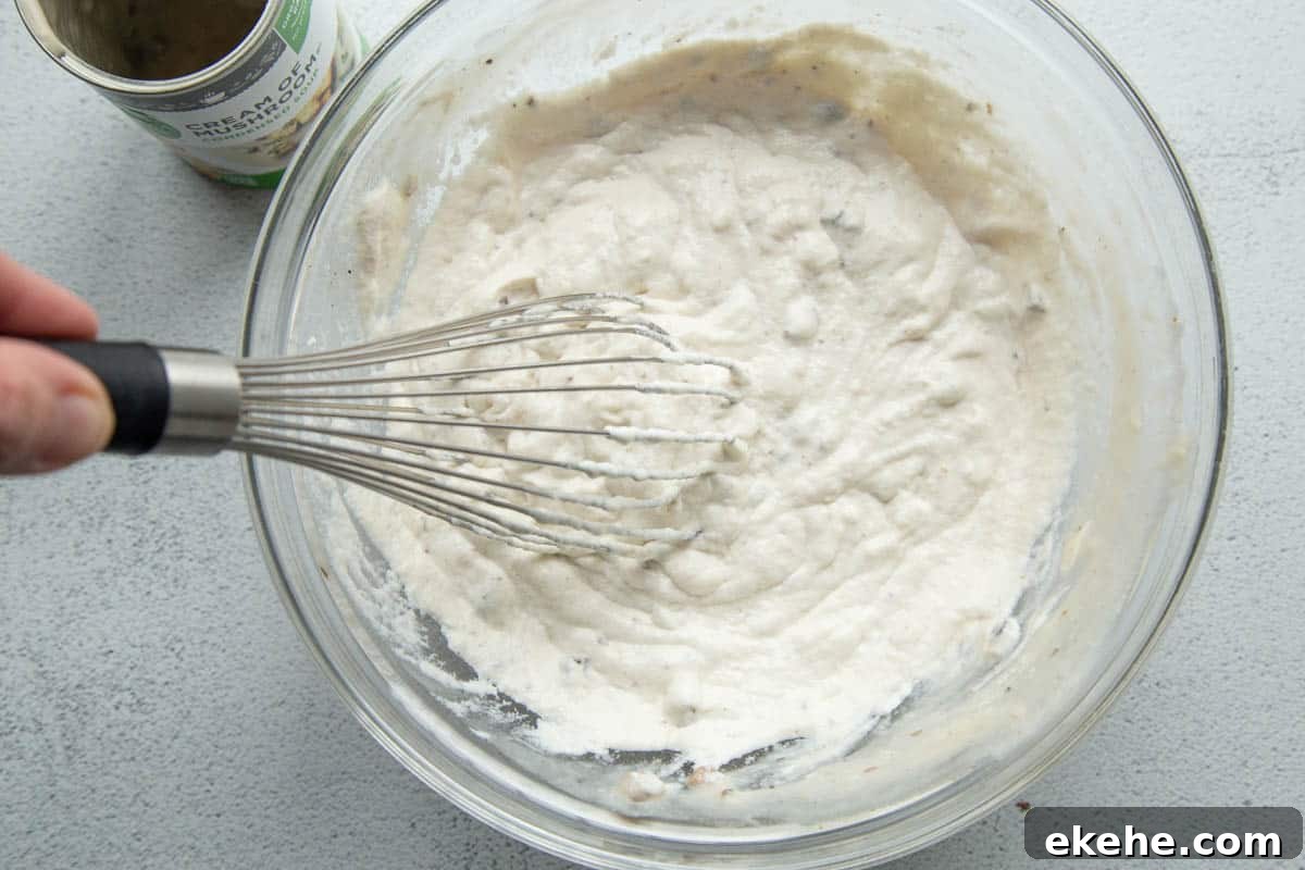 cream of mushroom soup and sour cream in a glass bowl with a whisk.