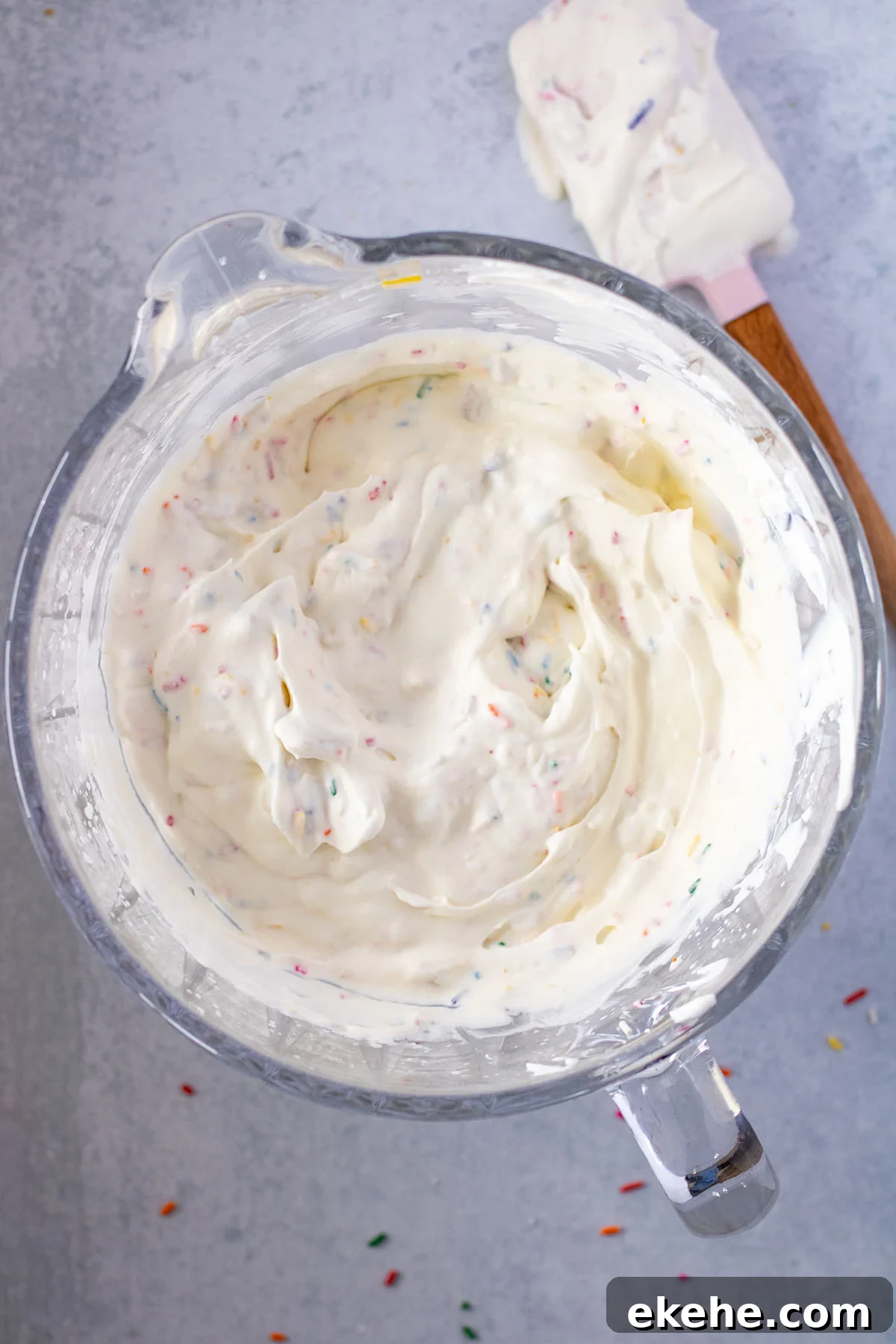 Chopped Oreos and sprinkles folded into ice cream in mixing bowl.
