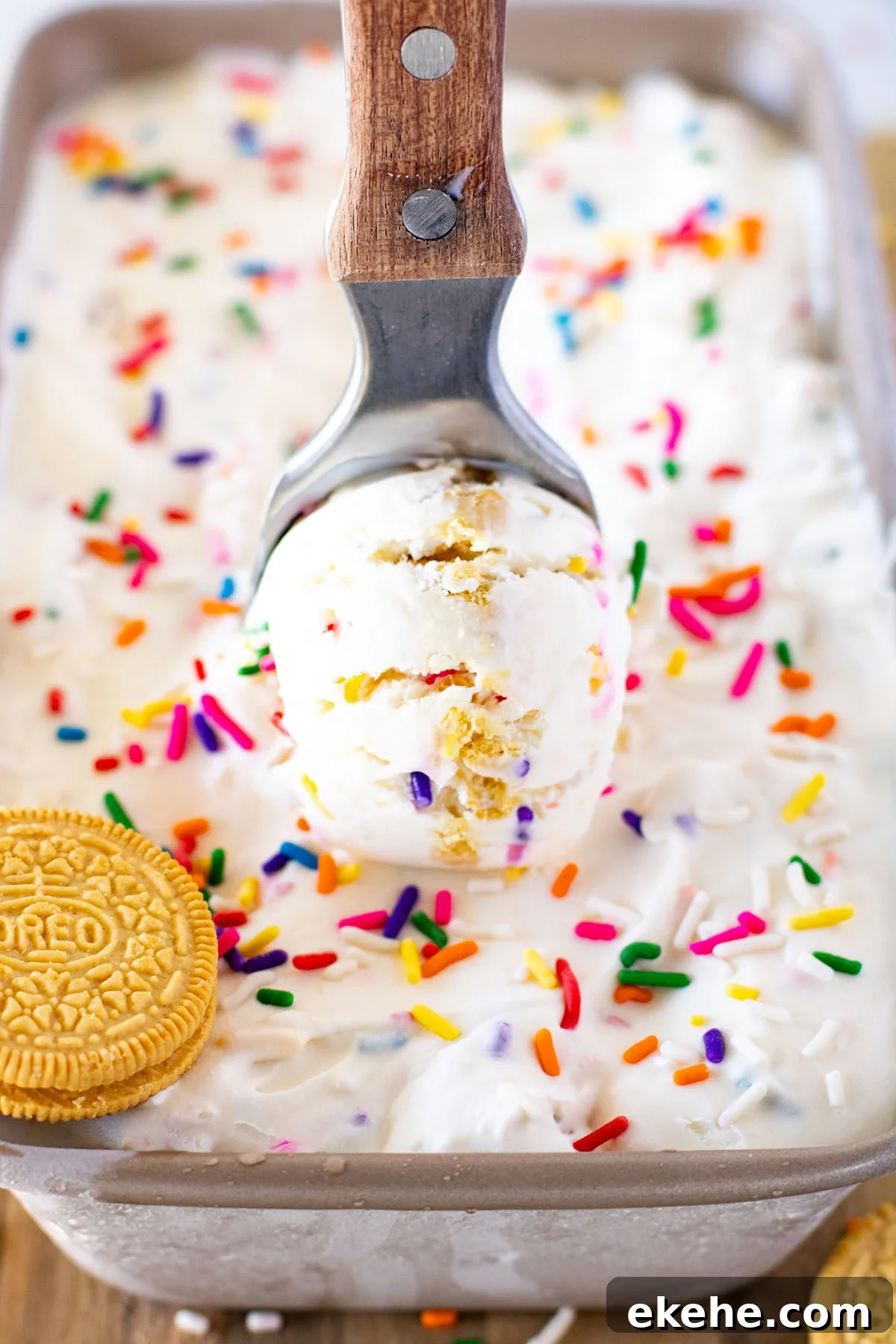 A scoop of Funfetti Golden Oreo Ice Cream being served out of the frozen ice cream in a metal loaf pan. 