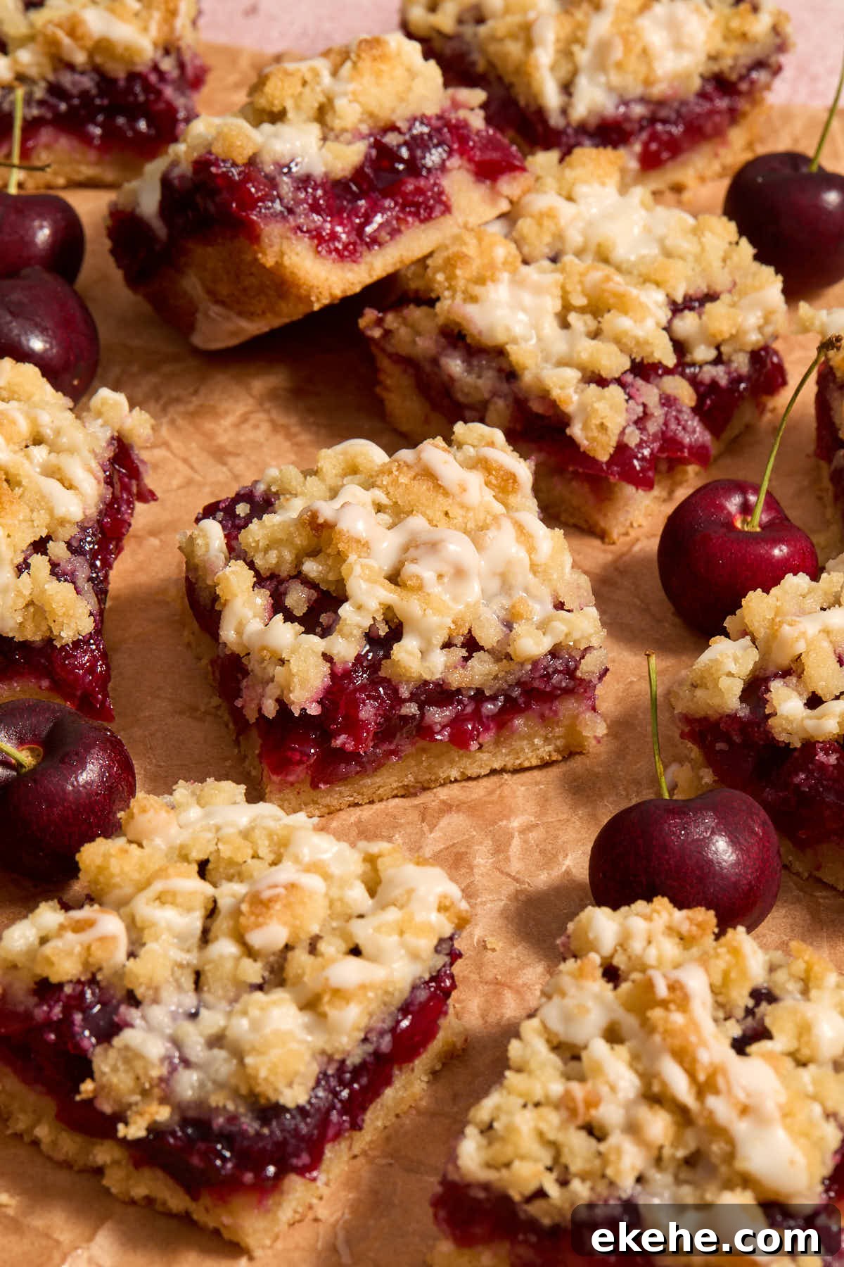 Cherry pie bars arranged on parchment with cherries around them.