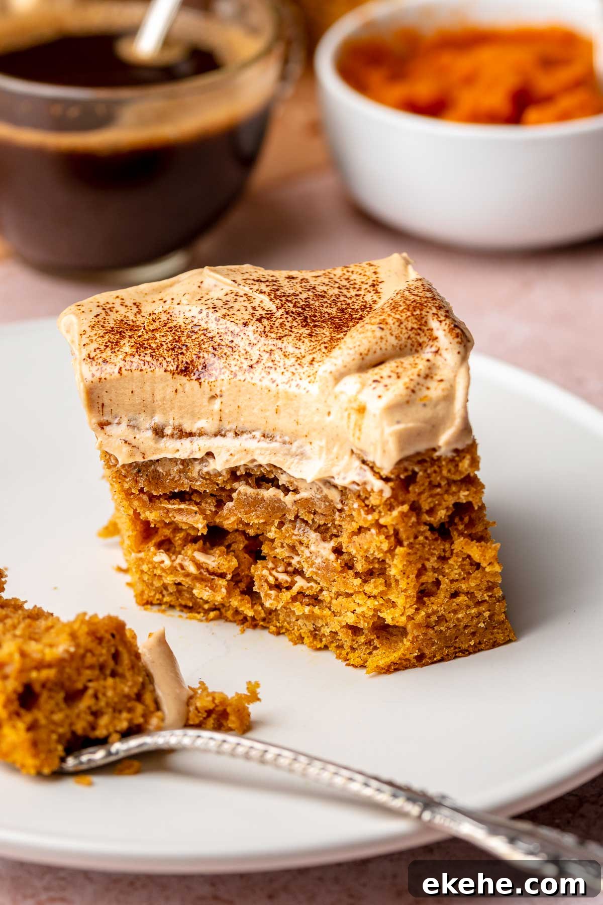 A square slice of pumpkin spice latte cake on a plate with a fork. A bite is removed.