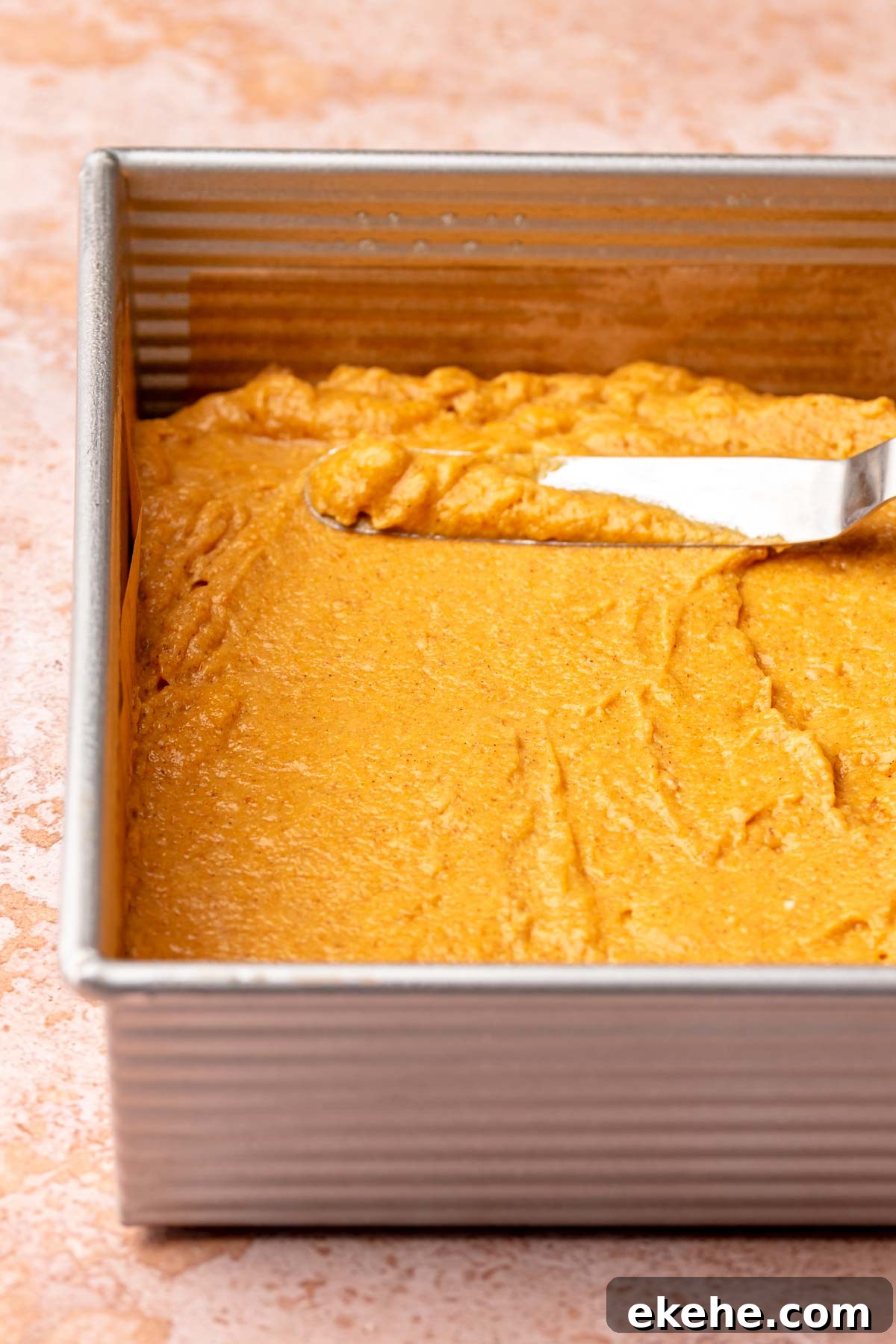 A spatula spreading pumpkin cake batter into a prepared square pan.