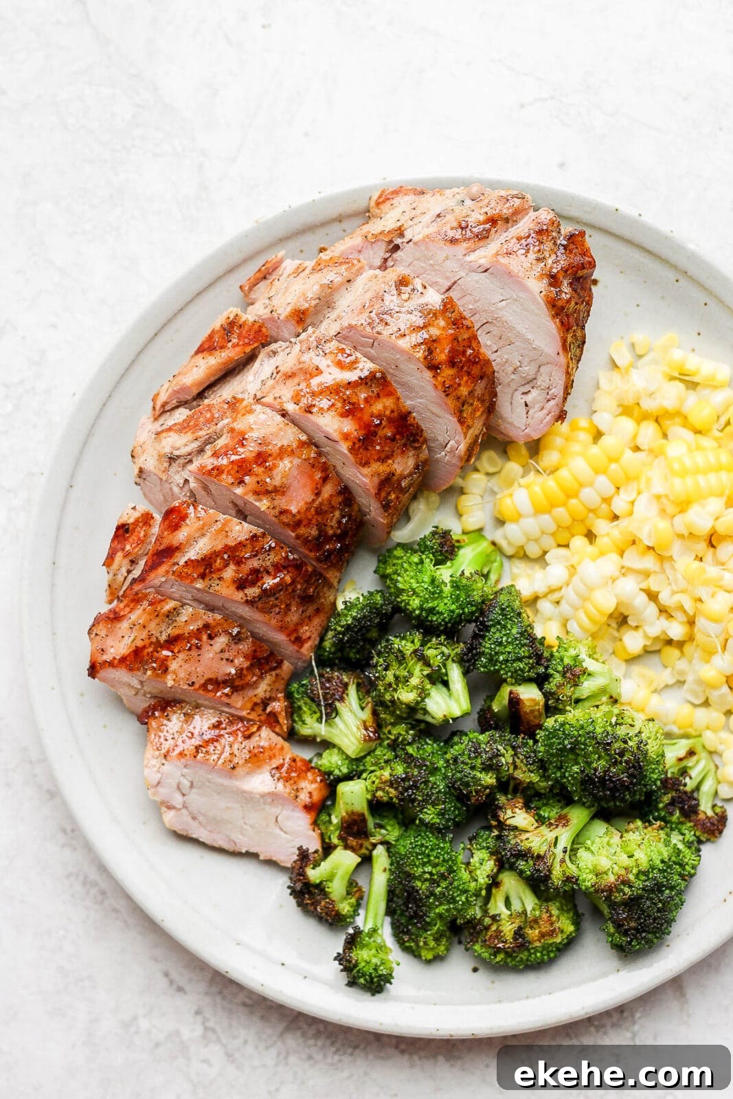 Smoked broccoli on a plate with sliced pork tenderloin and corn.