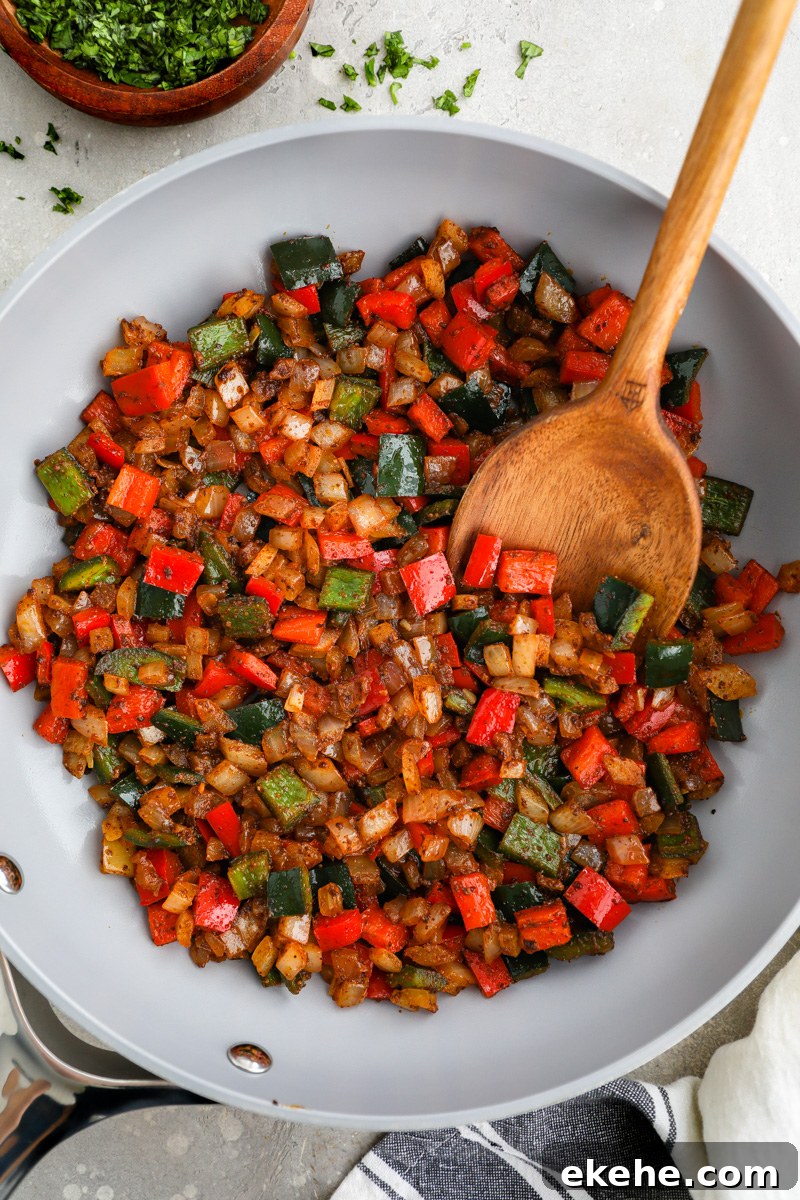 A large skillet filled with sauteed poblano pepper, bell peppers and white onion sitting next to a small bowl of chopped cilantro