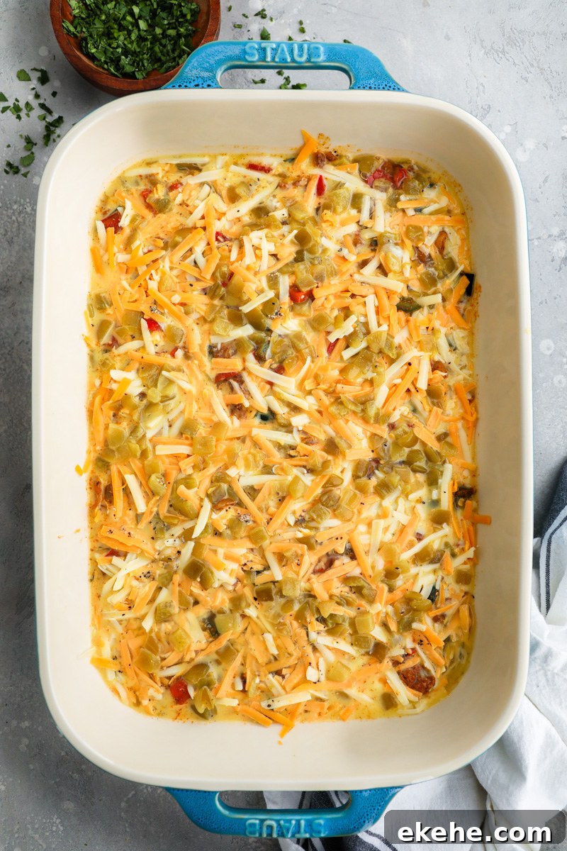 A 9x13 casserole dish filled with ingredients to make a chorizo and potato egg casserole topped with shredded cheese