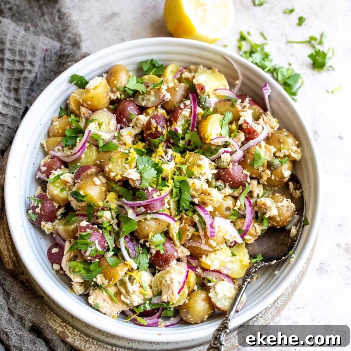 Tuna Potato Salad with red onions and a silver spoon in a white bowl. 