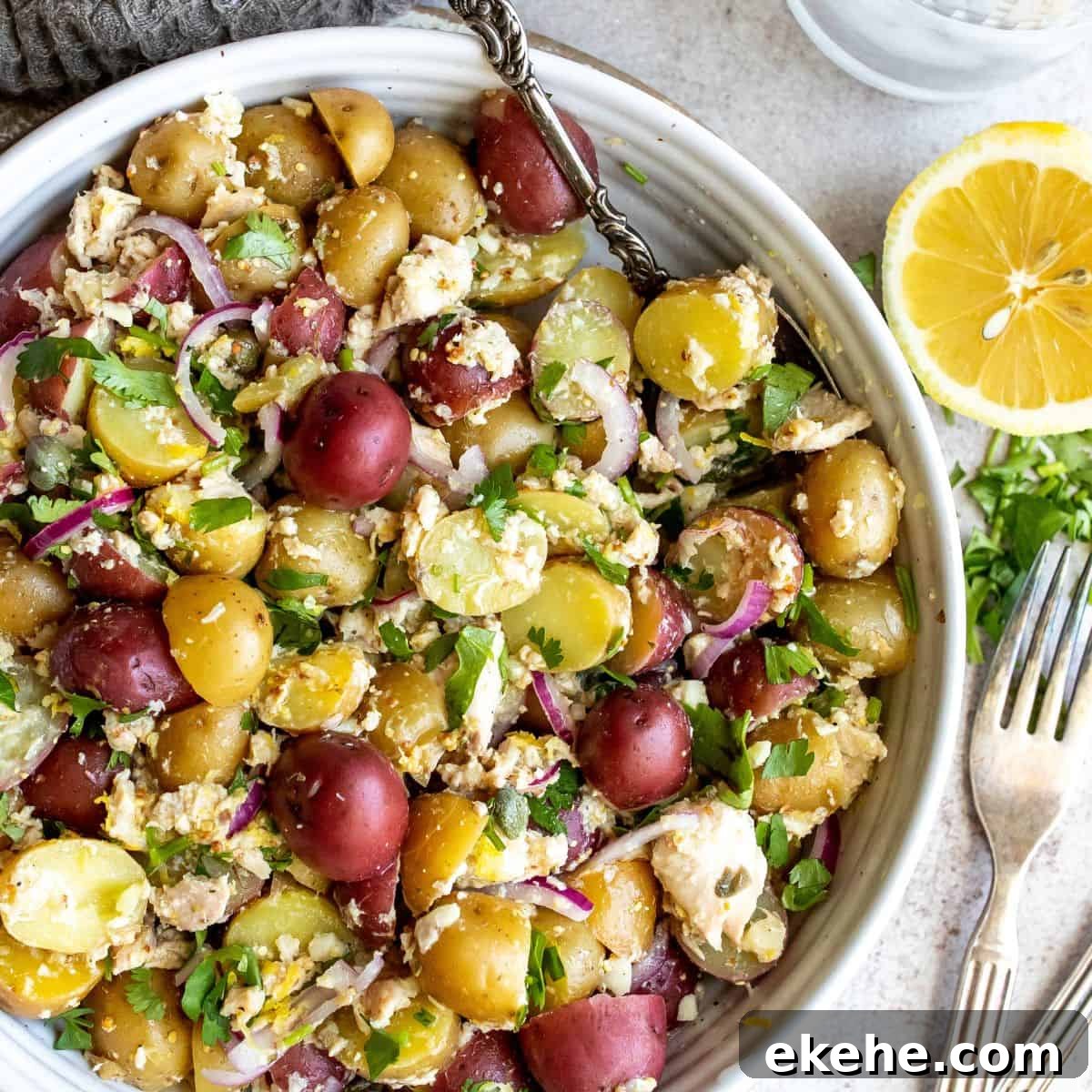 Tuna potato salad up close in a white bowl with a large silver spoon. 