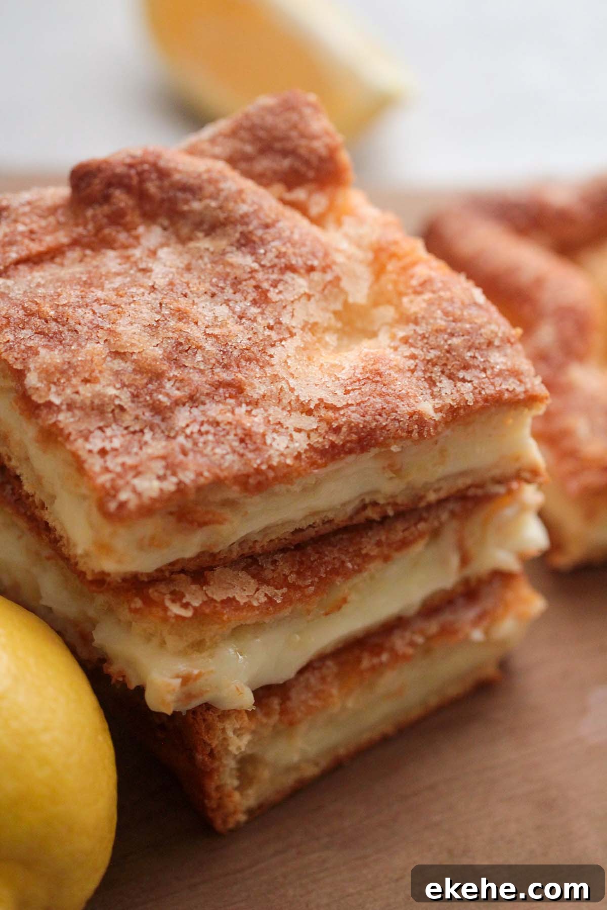 three lemon cream cheese bars stacked on a wooden board with a lemon on the side. 