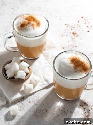 Two mugs of red cappuccino with some sugar cubes in a small bowl.