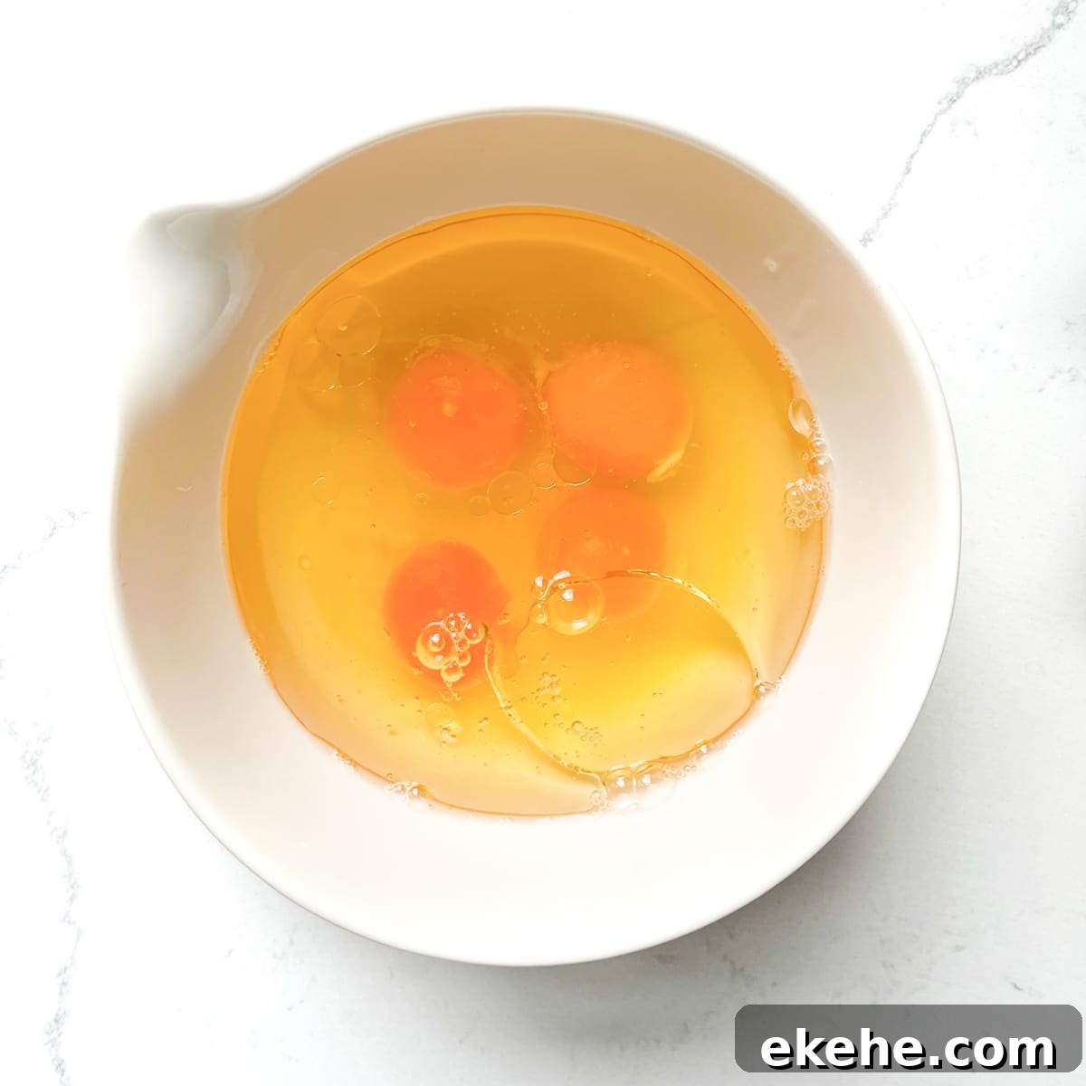 Eggs and oil added to a white bowl.