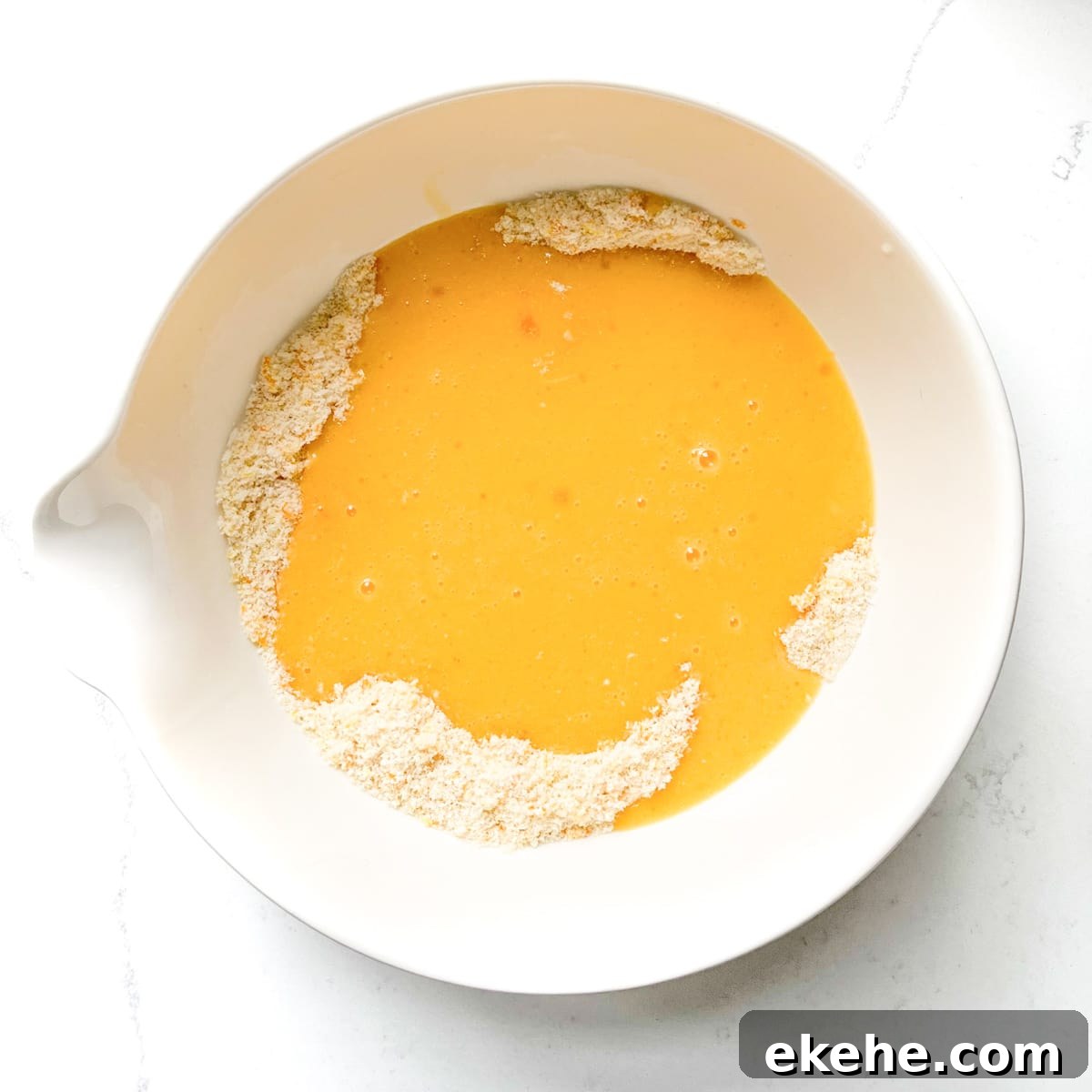 Adding the wet ingredients to the dry ingredients in a large white bowl.