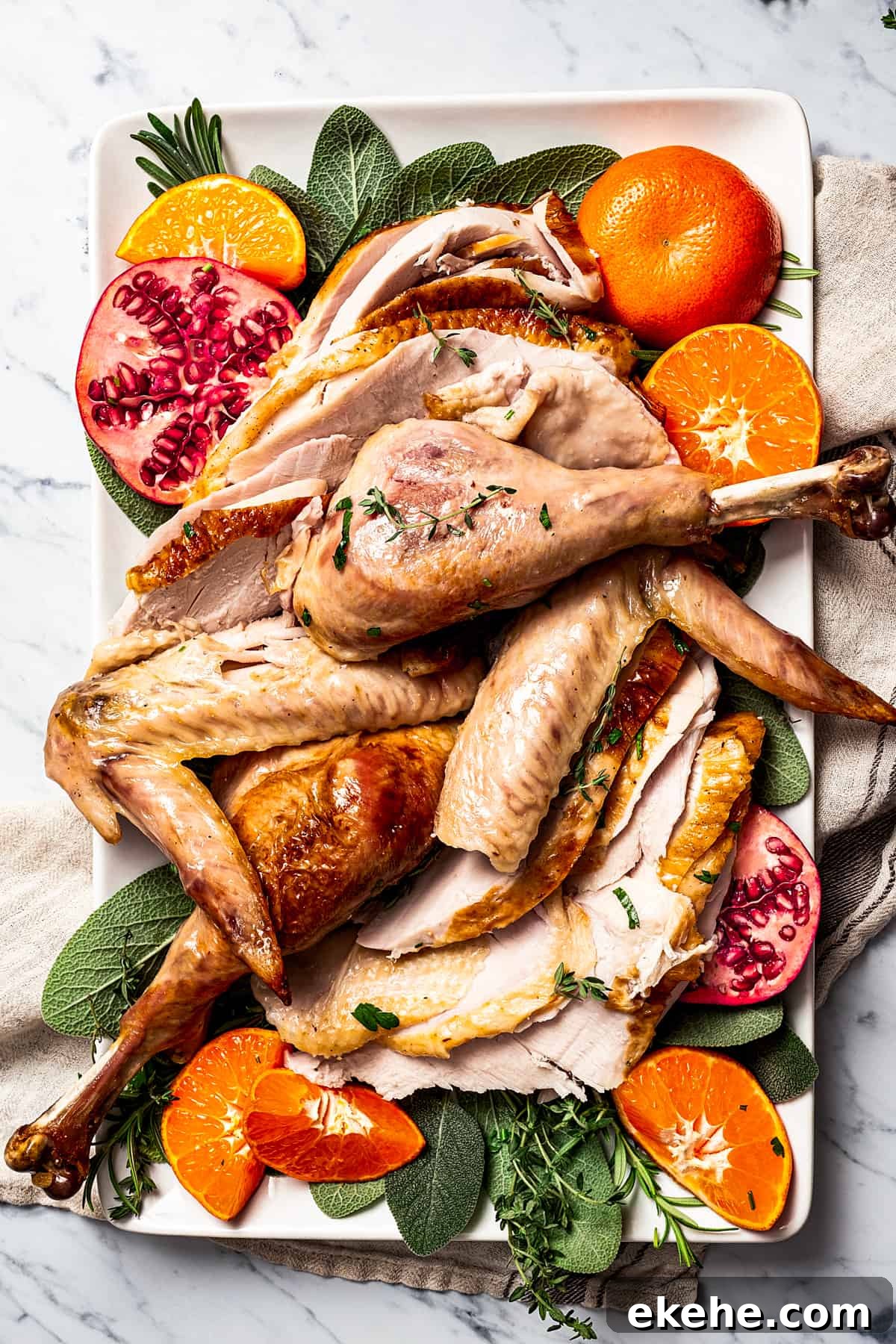 A serving platter of turkey drumsticks, wings, and breast meat, garnished with pomegranate and orange sections and fresh herbs.