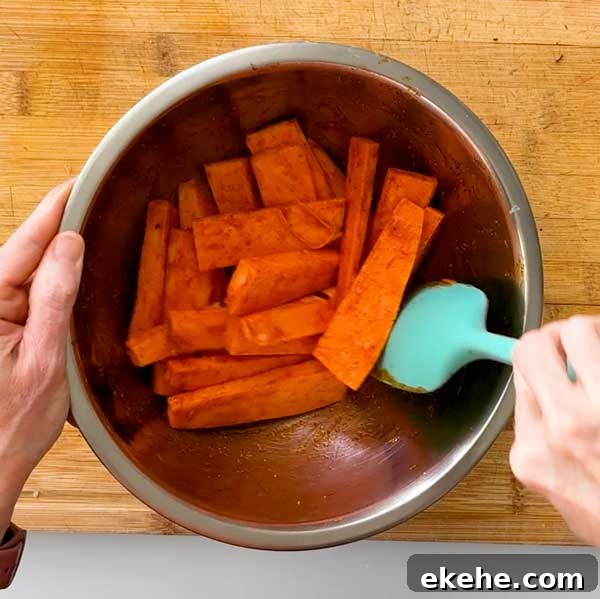 Tossing seasoned sweet potato wedges in a bowl for air fryer sweet potato fries.