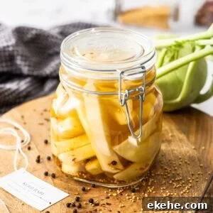 Jar of Pickled Kohlrabi, sitting on a round wooden board, with some herbs and spices around the edge.