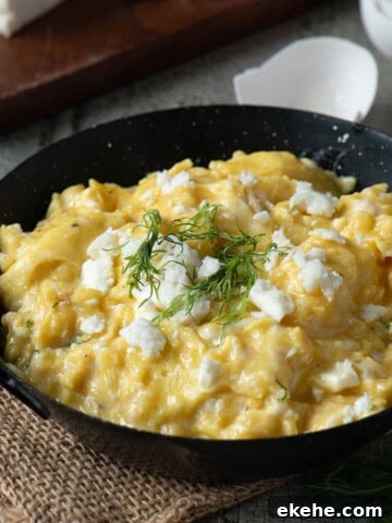 Scrambled eggs in a black skillet with feta and dill on top.
