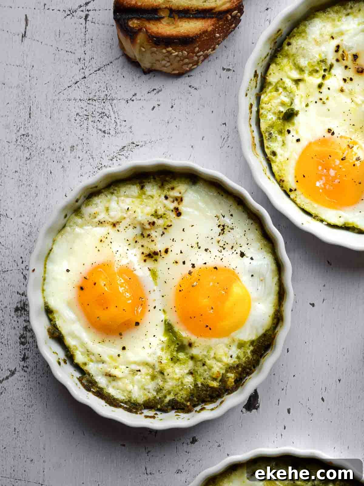 Overhead view baked eggs with pesto in white ramekins.
