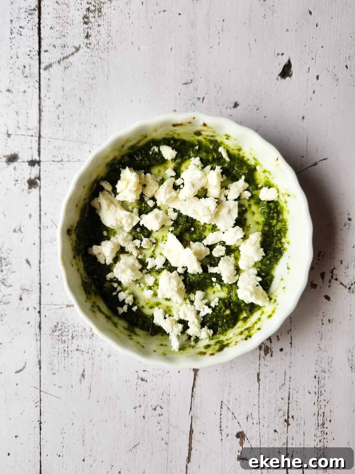 Pesto sauce and feta in a white ramekin.