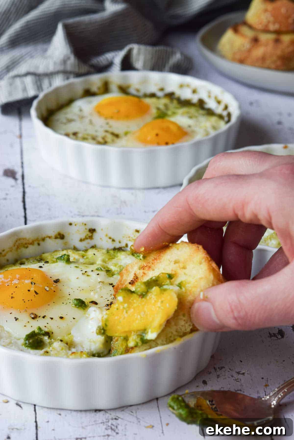 Bread being dunked in baked eggs in a ramekin.