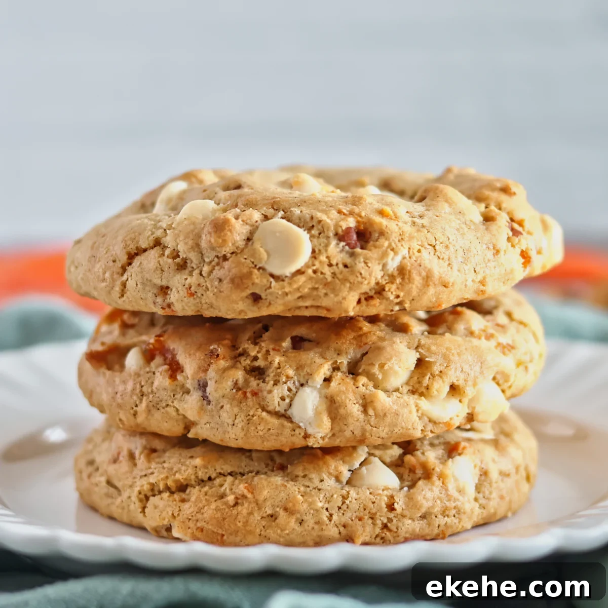 stack of 3 light brown or orange cookies with white chocolate chips on white plate.