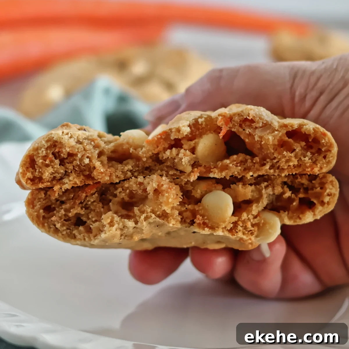 large orange cookie with white chocolate chips and shredded carrots broken in half and halves stacked on top of each other.