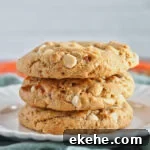 stack of 3 light brown or orange cookies with white chocolate chips on white plate.
