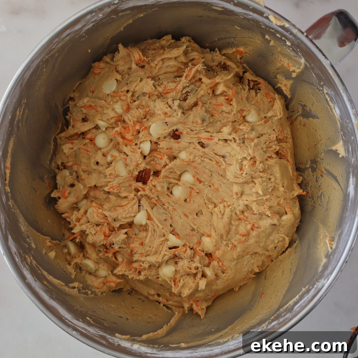 light brown cookie dough with white chocolate chips and carrots in stainless steel bowl.