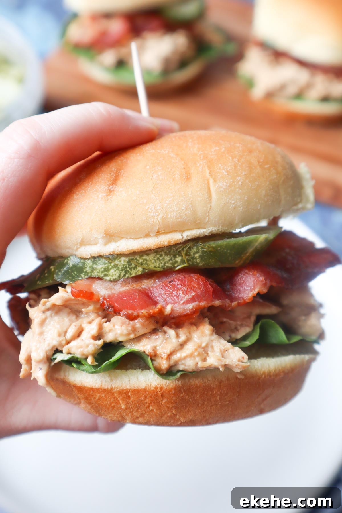 hand holding a chicken bacon ranch sandwich with ranch shredded chicken, lettuce, bacon, and pickle