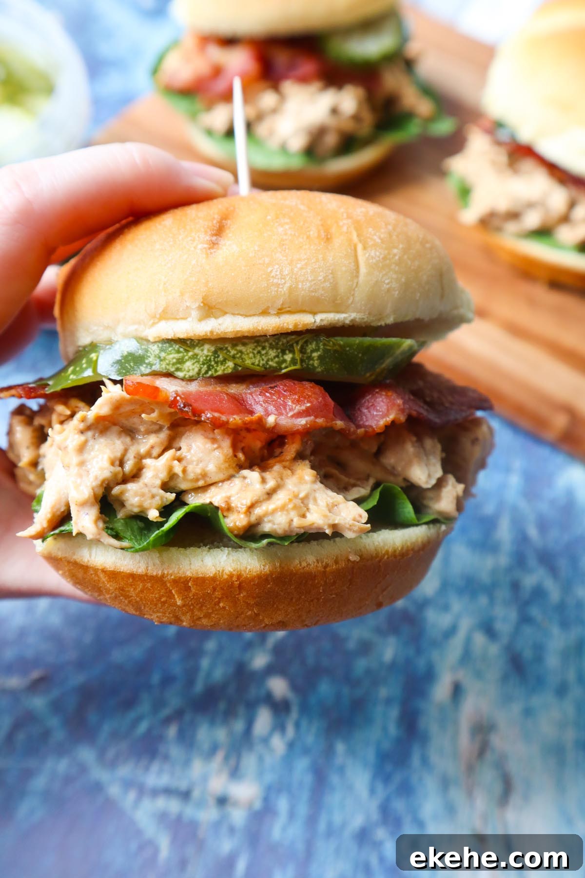 hand holding a chicken bacon ranch sandwich with ranch shredded chicken, lettuce, bacon, and pickle