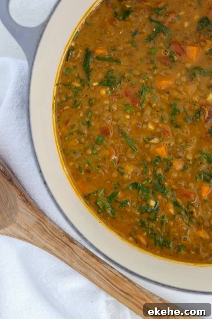 Hearty Lentil Soup with Roasted Butternut Squash, Kale and Bacon in a pot next to a wooden ladle