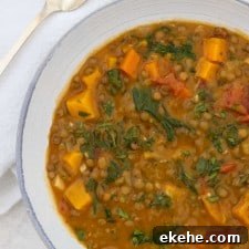 Close up of a bowl of Hearty Lentil Soup with Roasted Butternut Squash, Kale and Bacon next to a spoon and napkin