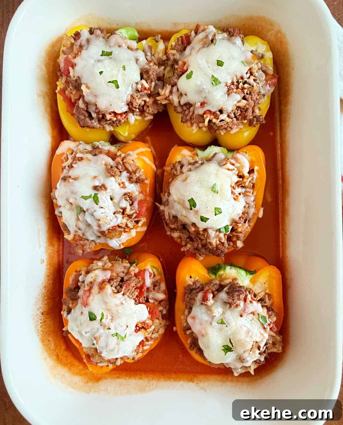 bell peppers stuffed with beef and rice with tomato sauce in baking dish.