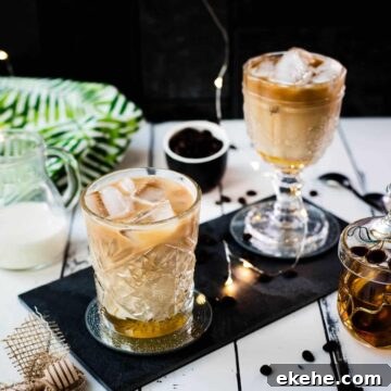 Two gorgeous glasses filled with iced honey latte placed on black slate plate.