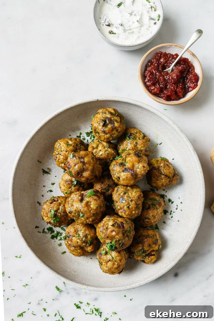 A bowl of Baked Chicken Kofta garnished with chopped cilantro with raita and chutney on the side.